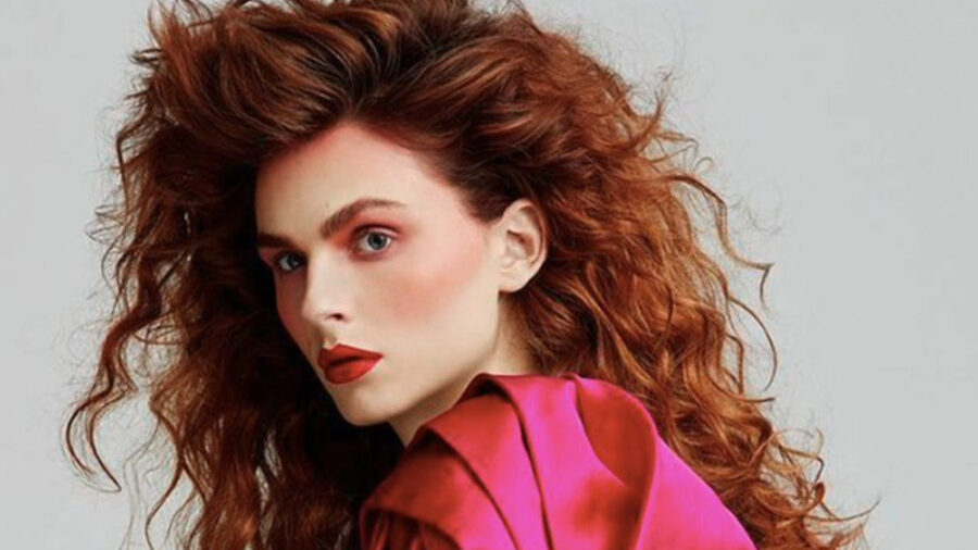 Andreja Pejić poses in profile wearing a red satin sleeve top, shot for ELLE Russia in London, December 2019.