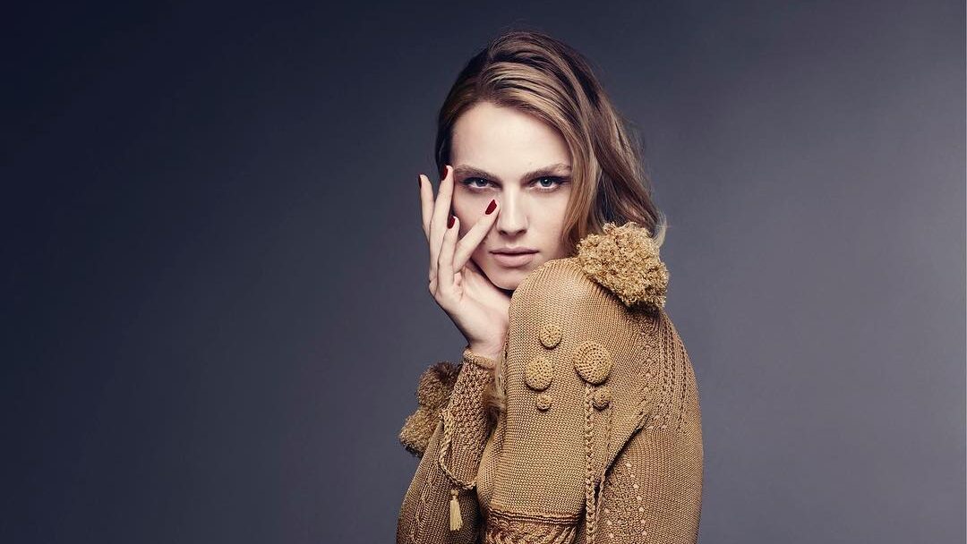 Andreja Pejić in a sculptural, gold-textured Giles Deacon gown, posing gracefully in a studio editorial portrait.