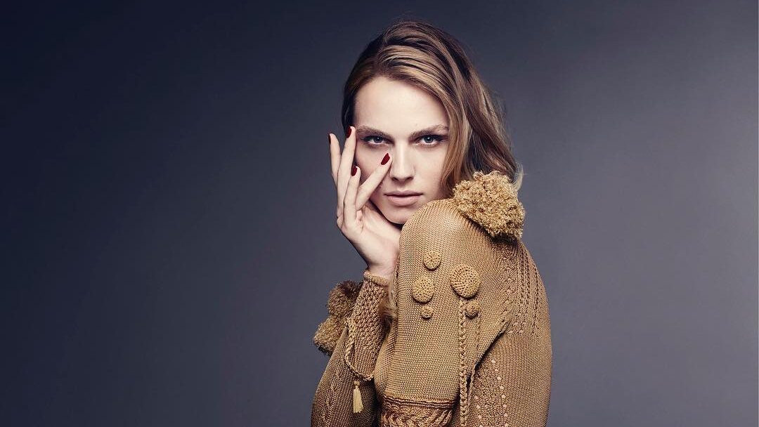 Andreja Pejić portant une robe sculpturale à texture dorée signée Giles Deacon, posant avec grâce dans un portrait éditorial en studio.