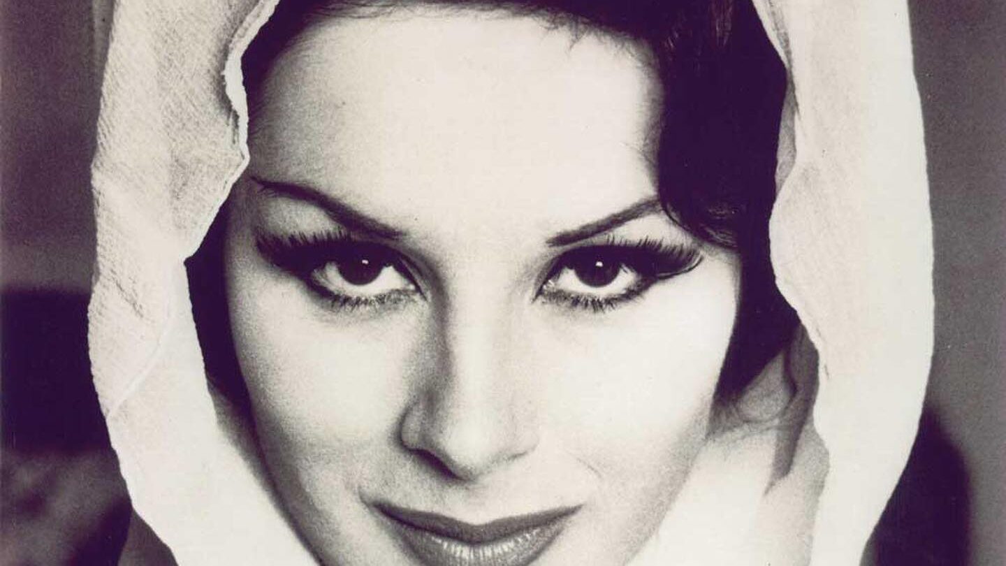 Black-and-white close-up portrait of April Ashley wearing a light-colored scarf over her head.