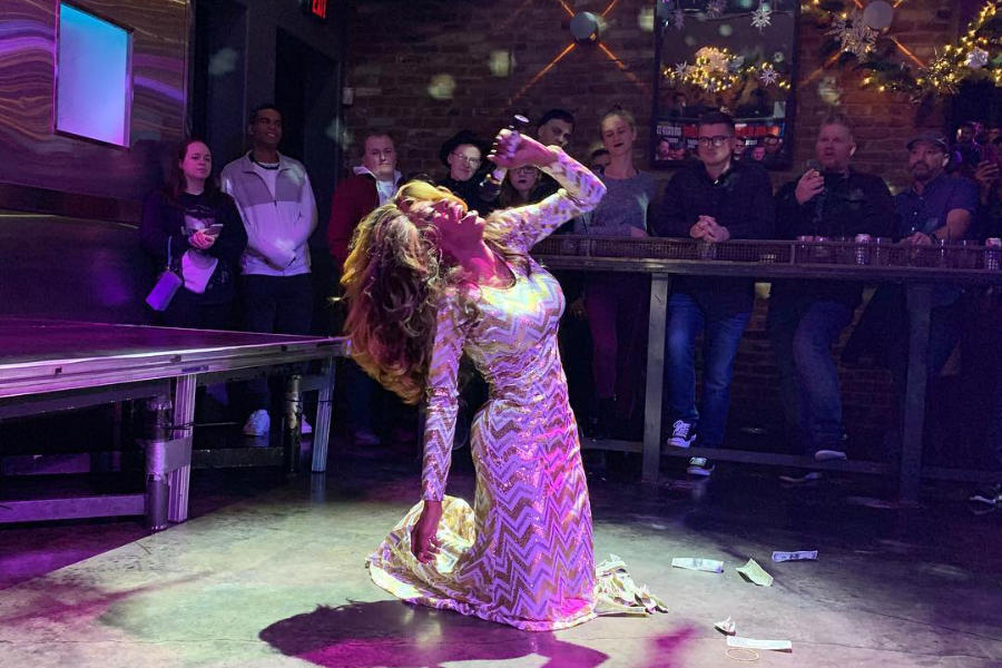 Drag queen Jasmine Masters performing at Badlands Sacramento, dazzling in a gold dress, crowd cheering behind her.