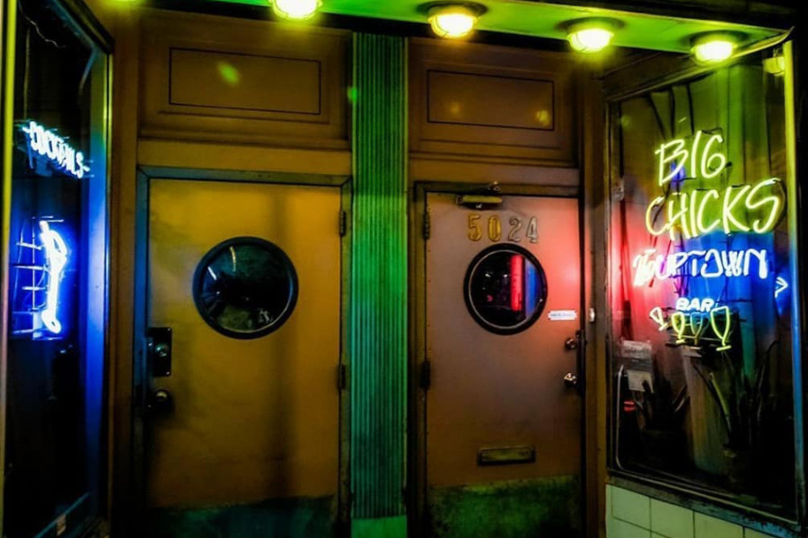 Neon-lit entrance of Big Chicks Bar in Chicago, with double brown doors and glowing signage at night.