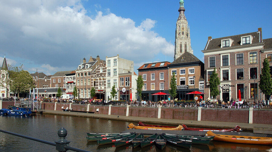 Boats docked at the port of Breda with historic buildings and the Grote Kerk tower in the background.