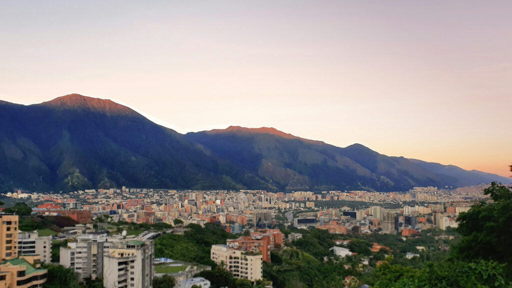 Vue de Caracas avec ses immeubles et le mont Ávila à l’arrière-plan sous un ciel rose.