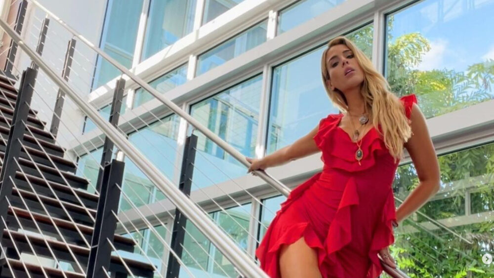 Carmen Carrera standing on a modern staircase, wearing a red ruffled dress.