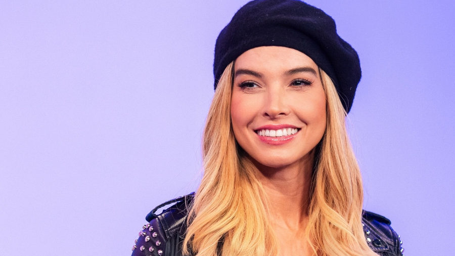 Carolina Gutierrez smiling on a TV set in Los Angeles, wearing a beret, studded jacket, and red top.