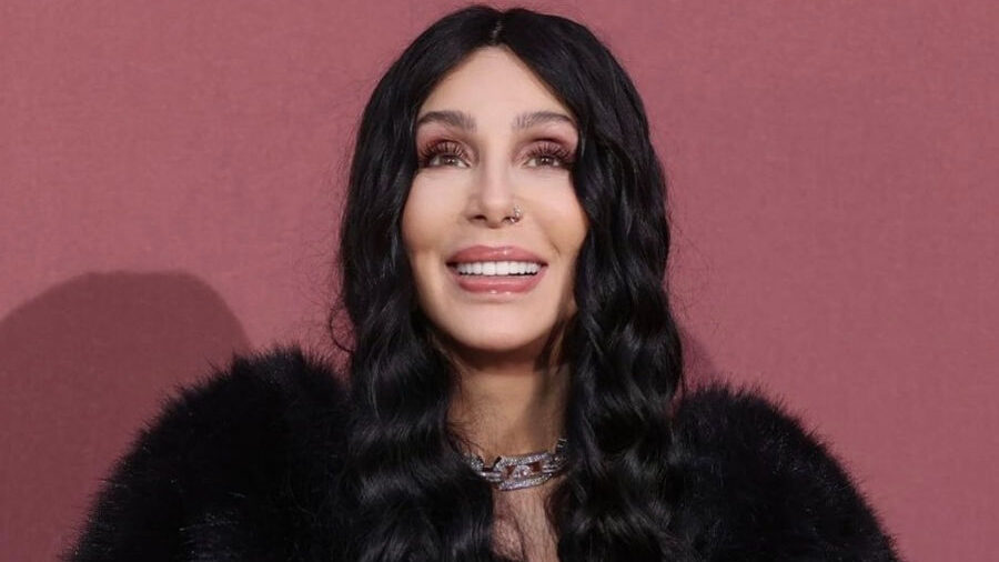 Singer Cher poses in Cannes, wearing a voluminous black fur coat, fingerless gloves, and a diamond necklace.