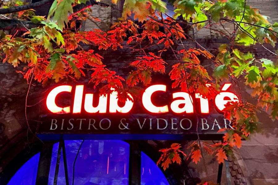 Illuminated Club Café sign in Boston framed by vibrant fall leaves.