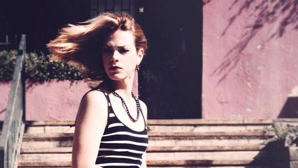 Daniela Vega jeune, assise sur des marches carrelées, robe rayée, cheveux au vent, photo partagée en 2023.