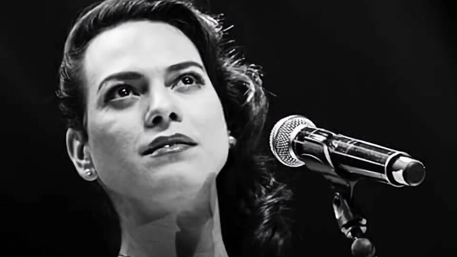 Photo en noir et blanc de Daniela Vega sur scène devant un micro, regard levé, éclairage doux.