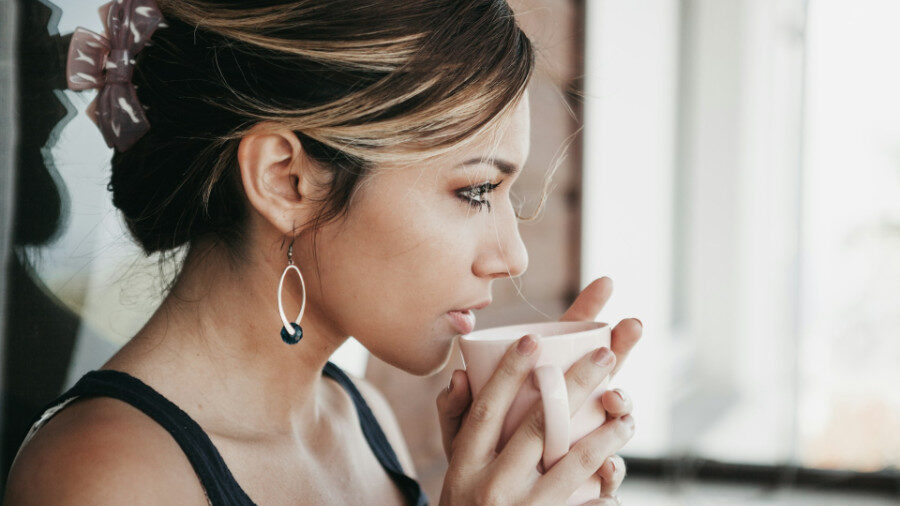 Jeune femme buvant dans une tasse blanche, portant une pince à cheveux et des boucles d'oreilles.