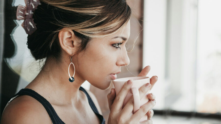 Mujer joven bebiendo de una taza blanca, con un clip para el cabello y aretes.