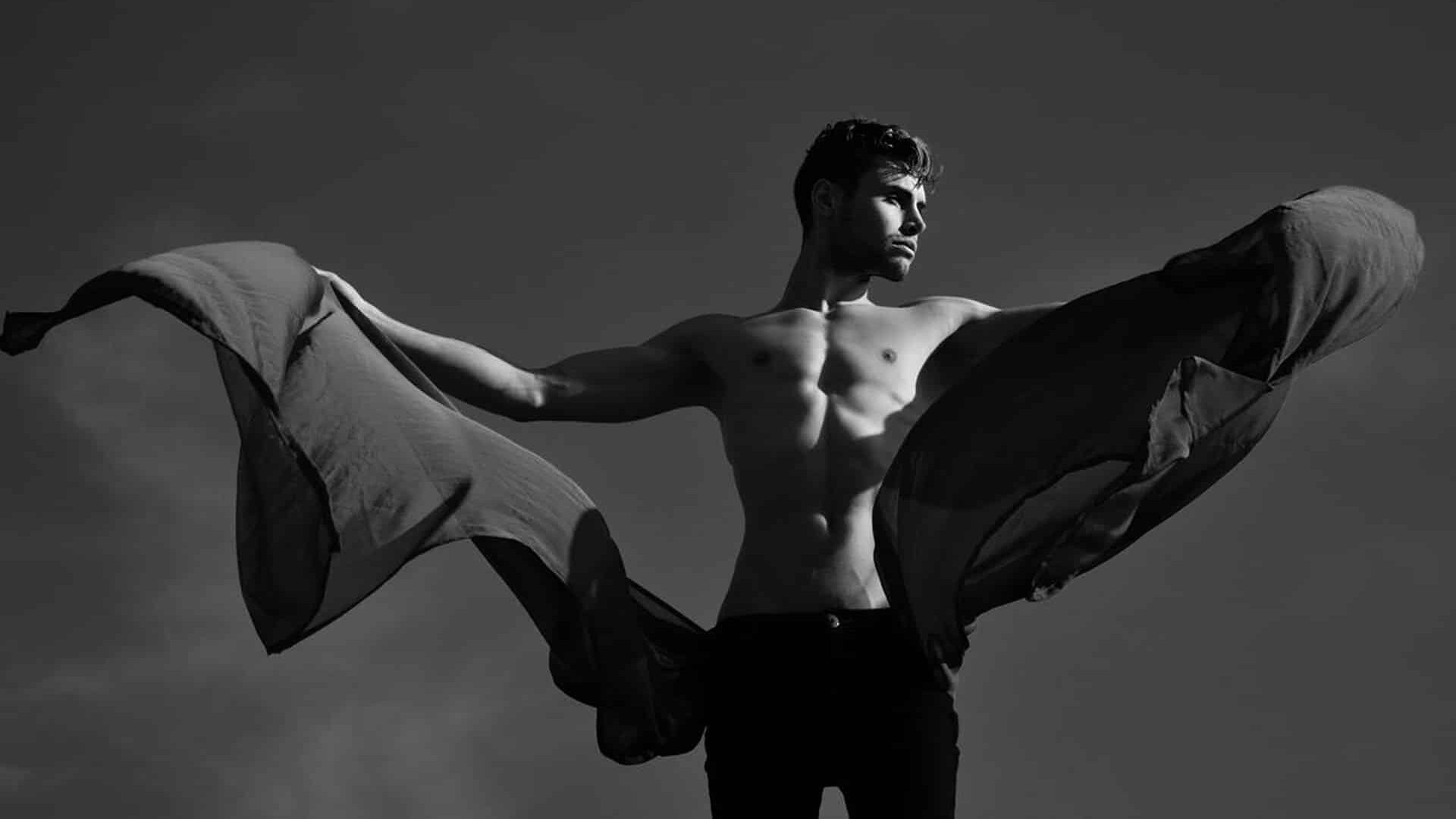 Artistic black-and-white image of a man with strong posture, extending fabric like wings.