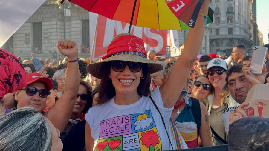 Smiling Florencia de la V at Plaza de Mayo, surrounded by protesters and rainbow flags.
