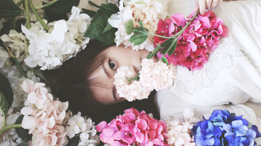 Mujer acostada entre flores coloridas con solo sus ojos visibles.