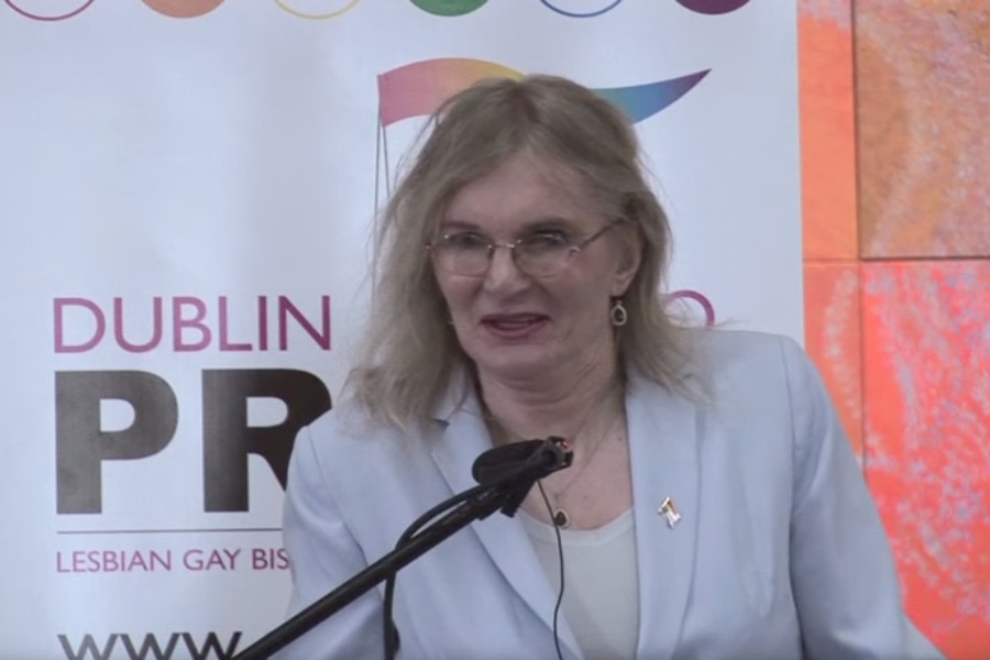 Lydia Foy speaking at a podium with a microphone in front of a Dublin Pride 2010 banner featuring rainbow colors.