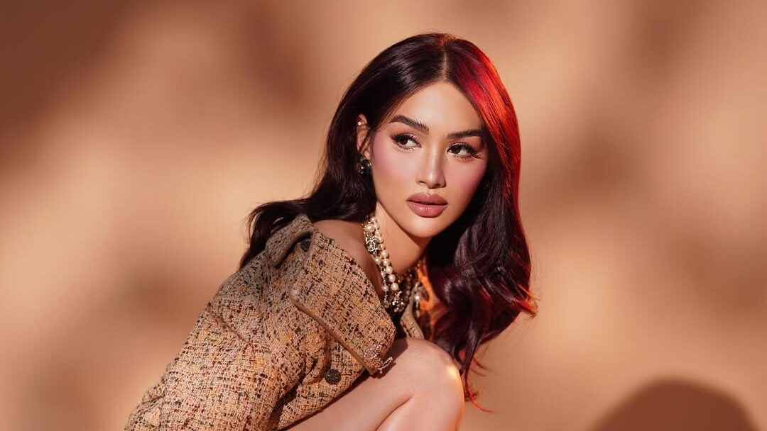 Francine Garcia crouching in a fashion editorial pose, wearing a textured brown jacket, black heels, and holding a gold handbag.