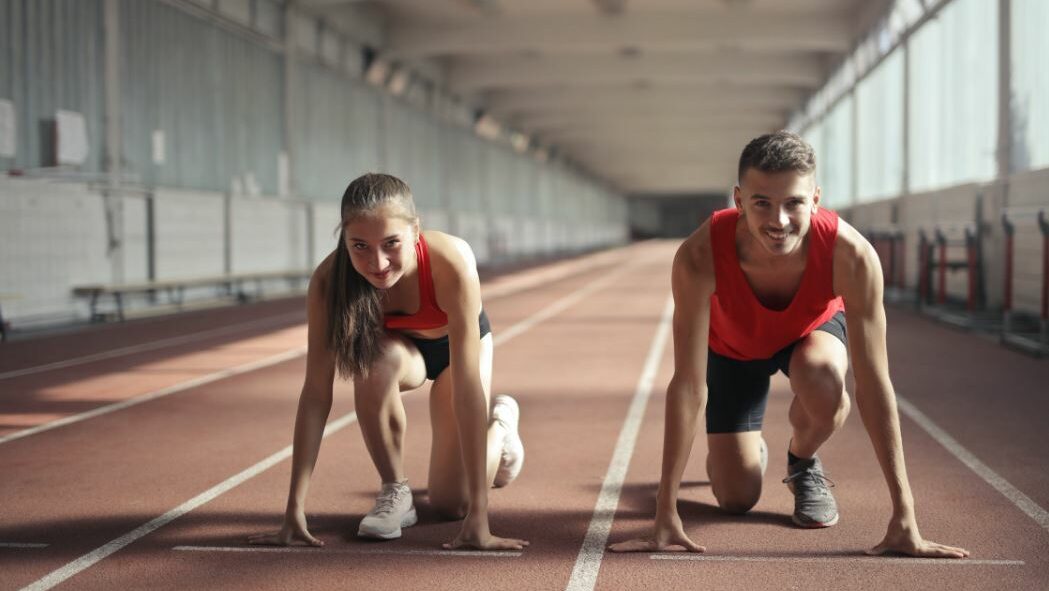 Deux athlètes en maillots rouges accroupis en position de départ sur une piste intérieure.
