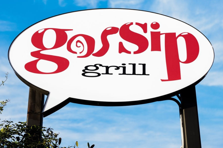 A large white Gossip Grill sign with red letters and a comic-style font is shown under a clear San Diego sky.