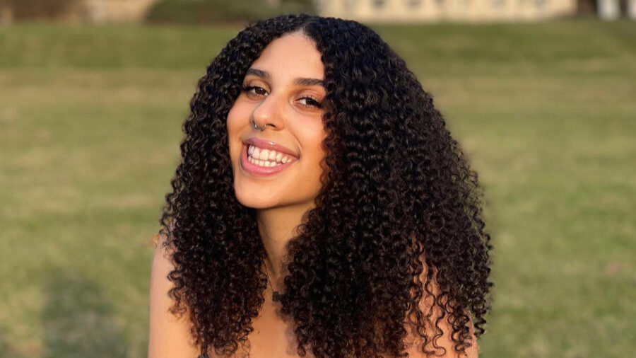 Portrait of Grace Dolan-Sandrino sitting on grass with buildings in the background.