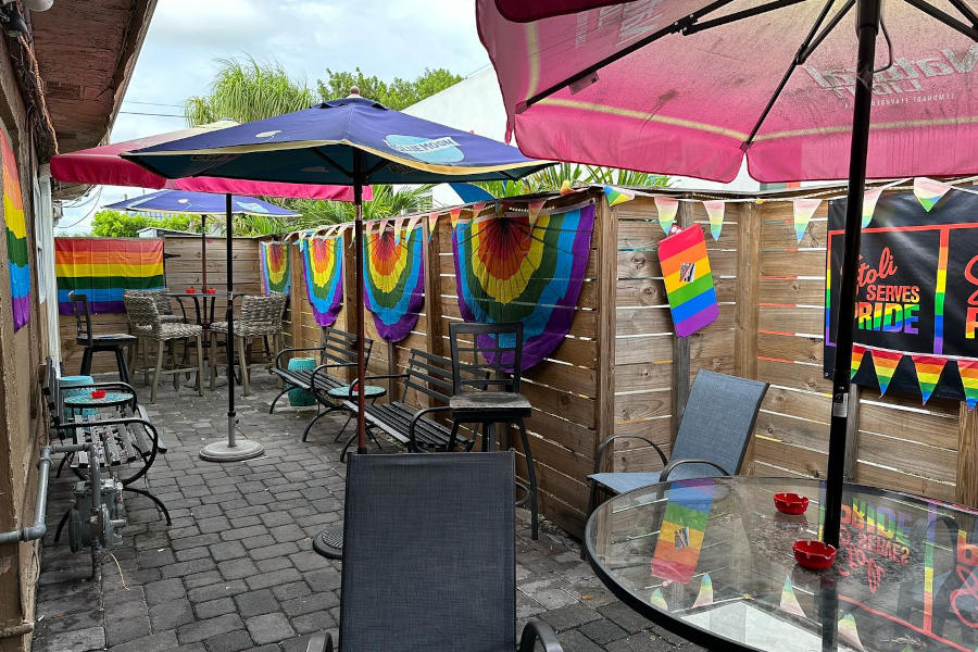 Relaxed post-rain view of Mad Hatter Lounge’s LGBTQ+ patio, filled with rainbow decor and cozy seating.