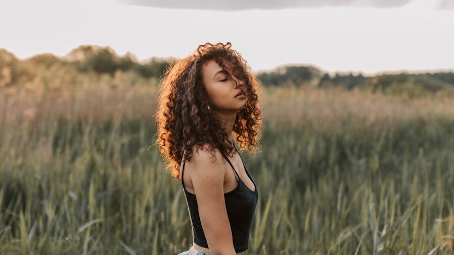 Portrait d’une jeune femme aux boucles volumineuses, portant un haut noir, entourée par la nature.