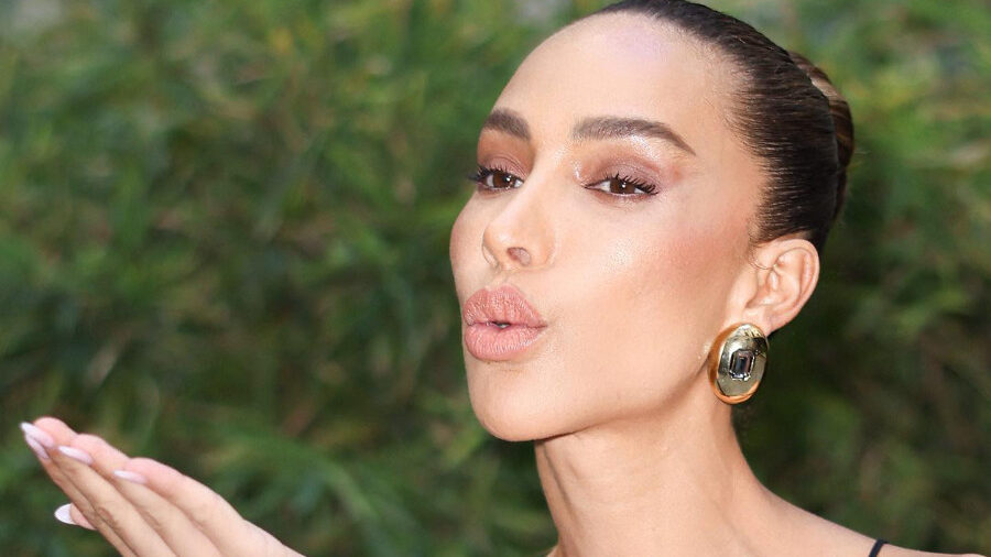 Ines Rau blowing a kiss outdoors, wearing a black top with gold earrings, in a photo shared October 2, 2023.
