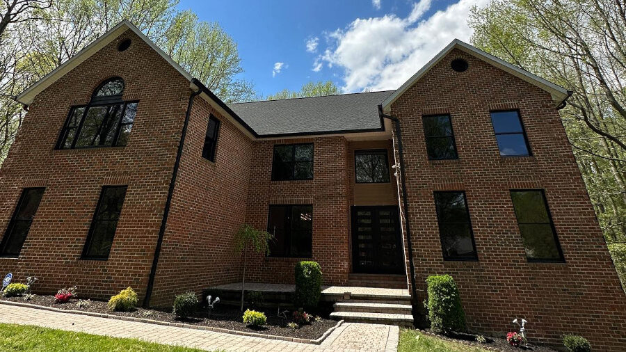 Maison en briques avec fenêtres à cadres noirs, fraîchement nettoyée, sous un ciel bleu partiellement nuageux dans le Maryland.