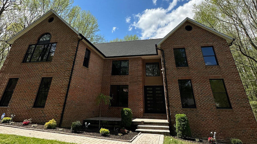 Brick house with black-framed windows, freshly cleaned, under a partly cloudy blue sky in Maryland.