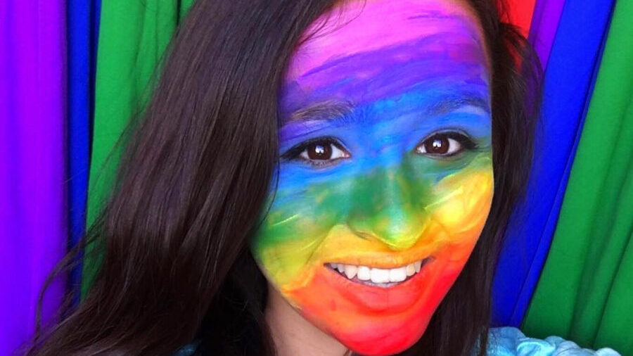 Jazz Jennings souriant devant un fond arc-en-ciel, le visage peint aux couleurs de la Pride.