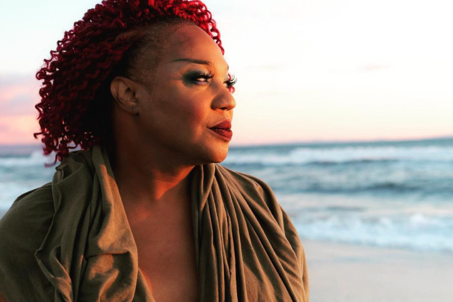 Jazzmun standing on a beach at sunset, wearing a brown draped outfit and looking into the distance.