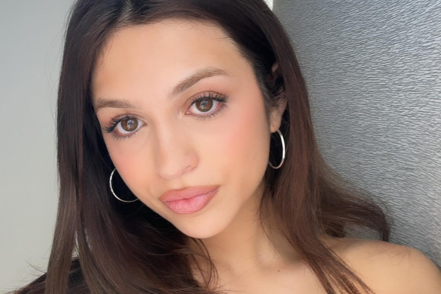 Selfie of actress Josie Totah, wearing hoop earrings and a black top, with long brown hair and soft makeup.
