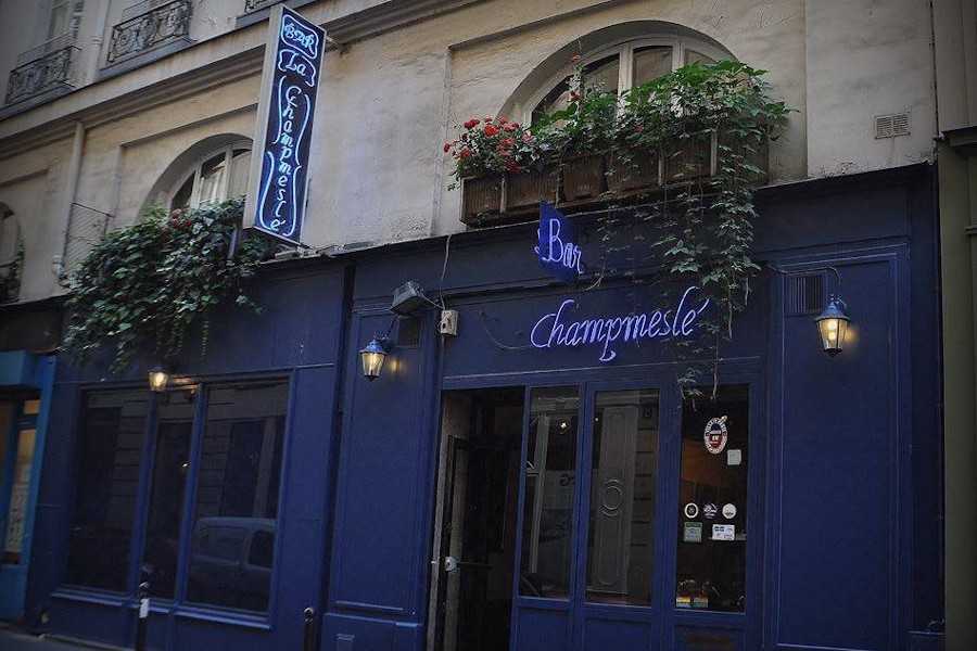 Exterior of Le Champmeslé bar in Paris, with blue walls, neon signage, and window planters above the entrance.