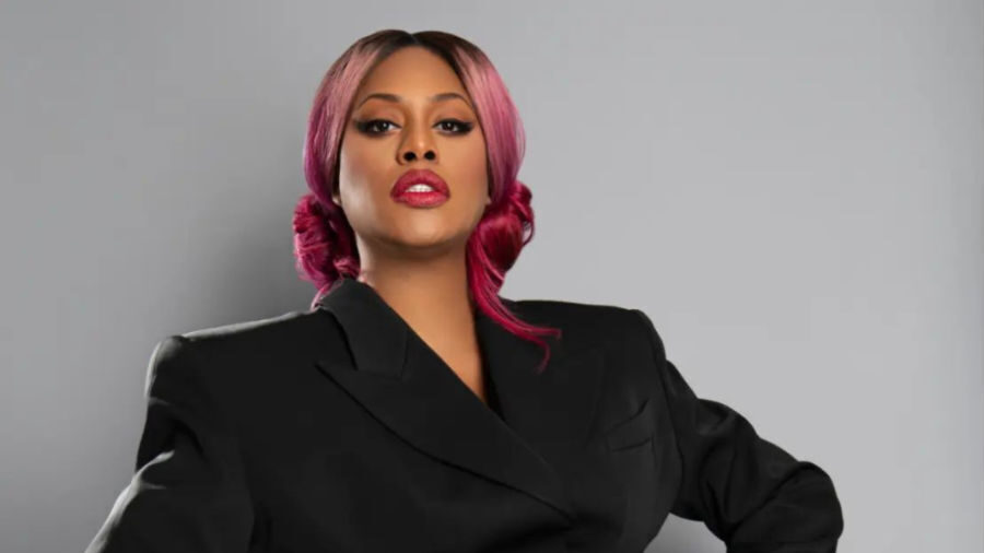 Laverne Cox in a black tailored blazer-dress with cutout detail, striking a confident pose.