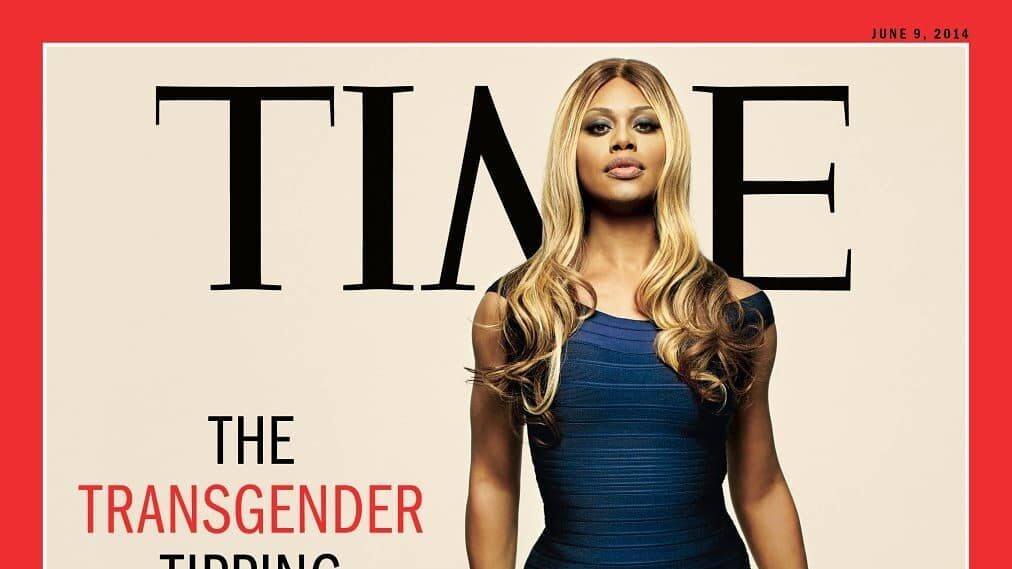 Laverne Cox poses confidently in a form-fitting dark blue dress on the June 9, 2014 cover of TIME magazine. The headline reads “The Transgender Tipping Point” with a subheading “America’s next civil rights frontier.” Her hair is styled in soft waves, and she stands tall and poised against a pale beige background under the bold TIME logo.