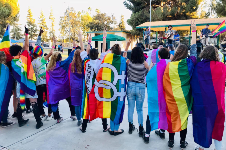 Pride participants in Bakersfield raise peace signs and rainbow flags during an outdoor LGBTQ.