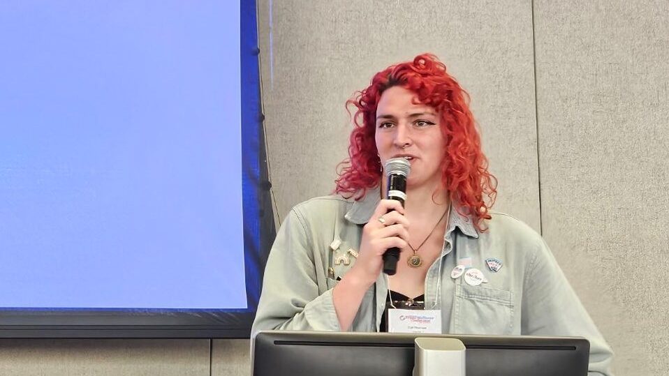 Lía Thomas de pie en un podio con un micrófono, hablando en una conferencia trans en 2024.