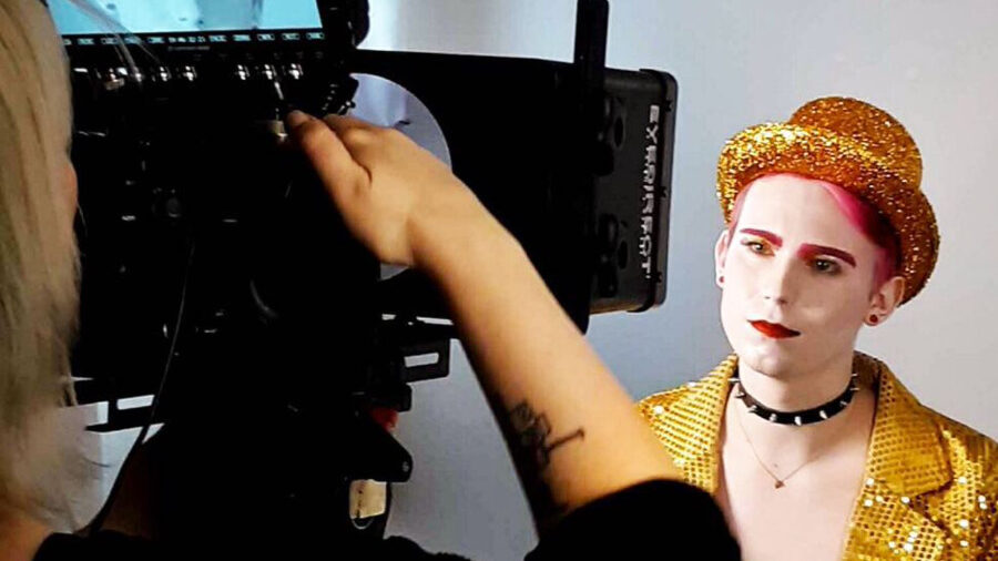 Lillian Lennon sits facing the camera in a gold sequin jacket and hat during a video shoot in 2019.