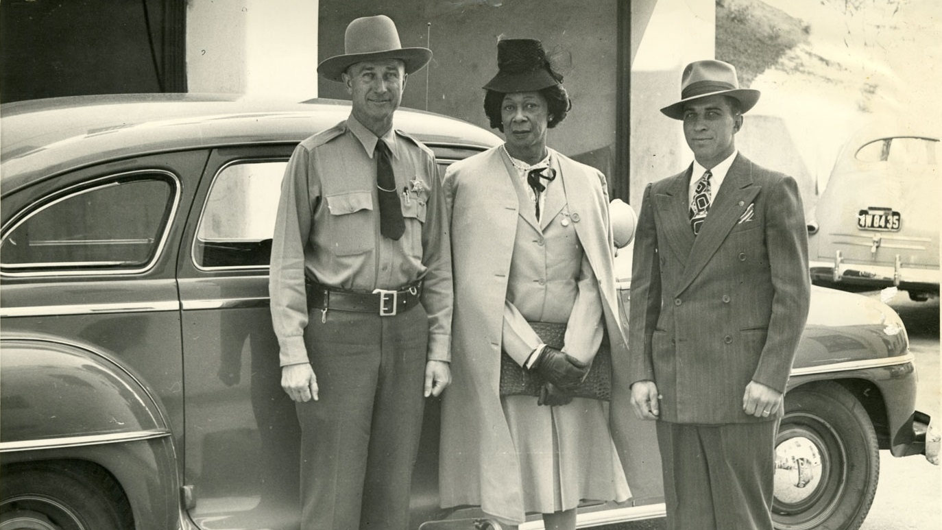 Lucy Hicks Anderson standing between Deputy Sheriffs H.E. Bowman and Charles Salig in front of a vintage car, circa 1945, in Ventura County, California.