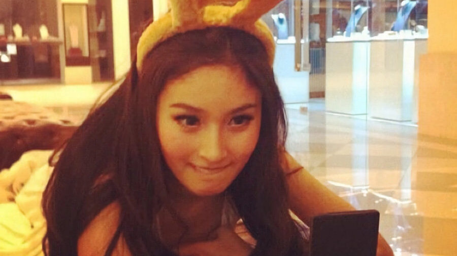 Close-up of Nong Poy looking at a phone while wearing bunny ears in a warmly-lit store.