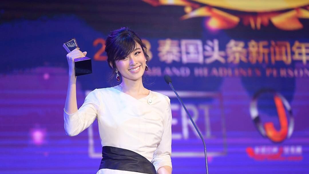 Nong Poy in white dress holding her Person of the Year award onstage at Siam Paragon.