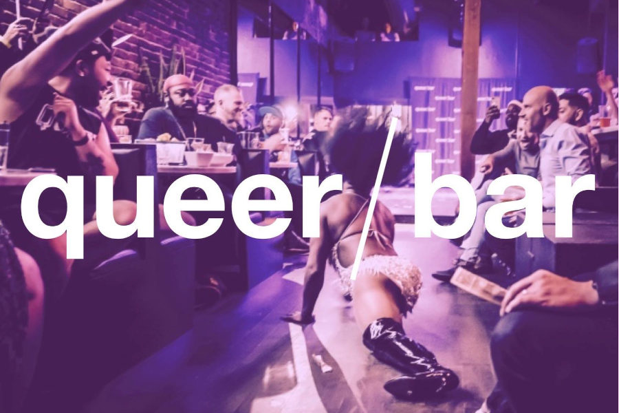 View of Queer Bar’s interior with purple lighting and an energetic drag show in progress, audience engaged and clapping.