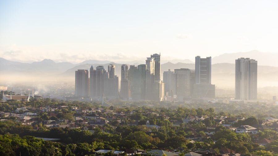 Aerial view of Quezon City, Philippines at sunrise with skyscrapers emerging from a light morning mist and mountains in the distance.