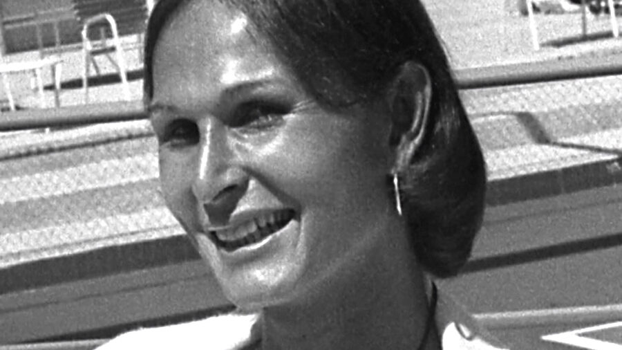 Renée Richards smiling during a 1976 press meeting at a Newport Beach tennis club, wearing earrings and a blouse.