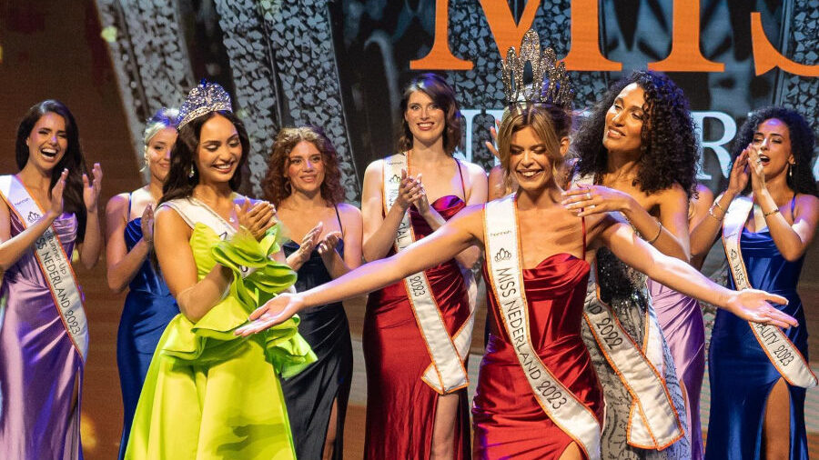 Rikkie Kollé smiling in a red gown as she is crowned Miss Nederland 2023 on stage with other finalists.