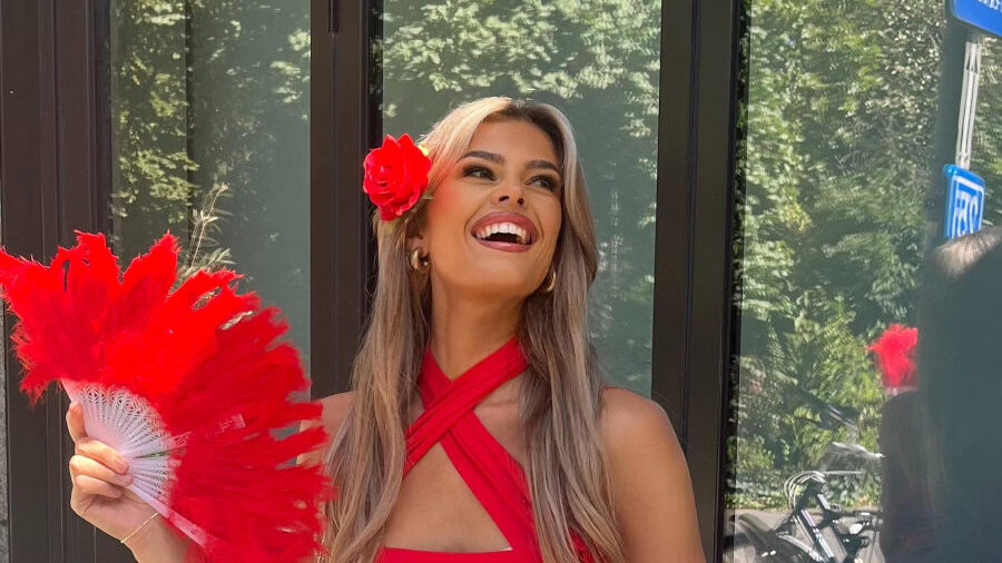 Rikkie Kollé souriante en tenue rouge avec une fleur, assise à une table durant l’Antwerp Pride 2024.