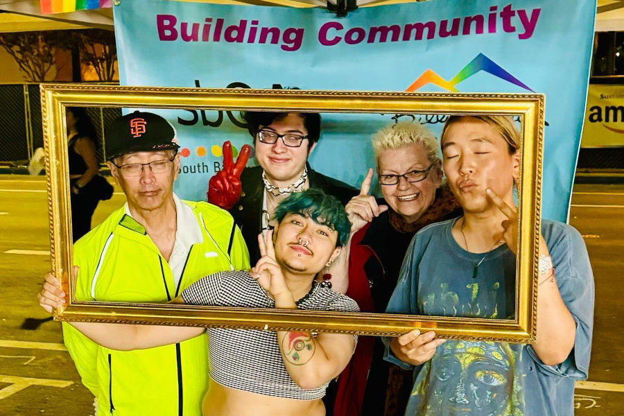 A joyful group from SbQA poses with a frame at their booth during Silicon Valley Pride 2024 in San Jose.