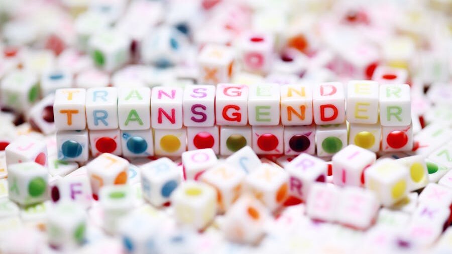 Close-up of colorful letter cubes spelling “TRANSGENDER” among scattered beads on a white background.