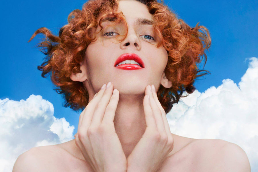 SOPHIE touching her neck, red lipstick, curly hair, photographed for “It’s Okay to Cry”.