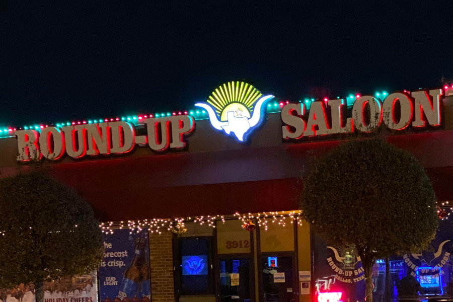 Front of Round-Up Saloon at night with red neon sign and festive string lights on the roof and windows.